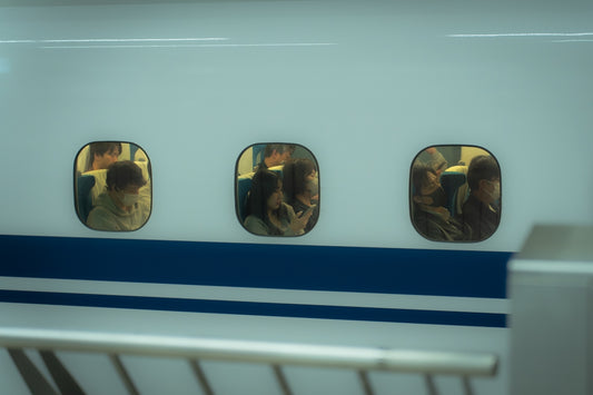 People are visible through three train windows.